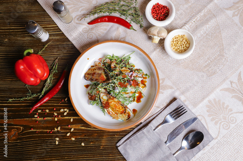 On a dark countertop, a light linen napkin, on a cutting board  Salad with mussels, rucola, red caviar, shrimps in a round dish, cutlery, pepper-salt steam, whole red pepper, hot pepper pod