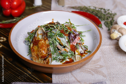 On a dark countertop, a light linen napkin, on a cutting board  Salad with mussels, rucola, red caviar, shrimps in a round dish, cutlery, pepper-salt steam, whole red pepper, hot pepper pod