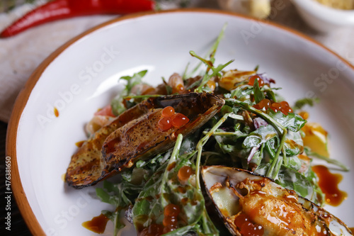 On a dark countertop, a light linen napkin, on a cutting board  Salad with mussels, rucola, red caviar, shrimps in a round dish, cutlery, pepper-salt steam, whole red pepper, hot pepper pod