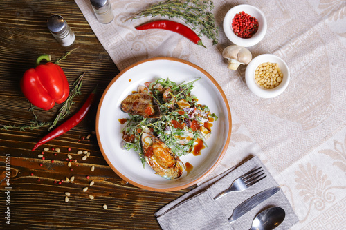 On a dark countertop, a light linen napkin, on a cutting board  Salad with mussels, rucola, red caviar, shrimps in a round dish, cutlery, pepper-salt steam, whole red pepper, hot pepper pod