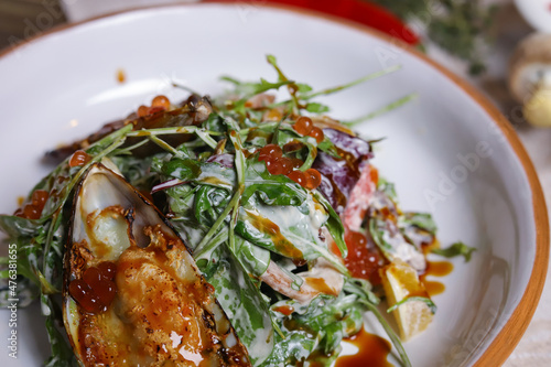 On a dark countertop, a light linen napkin, on a cutting board  Salad with mussels, rucola, red caviar, shrimps in a round dish, cutlery, pepper-salt steam, whole red pepper, hot pepper pod