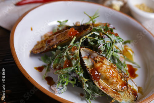 On a dark countertop, a light linen napkin, on a cutting board  Salad with mussels, rucola, red caviar, shrimps in a round dish, cutlery, pepper-salt steam, whole red pepper, hot pepper pod