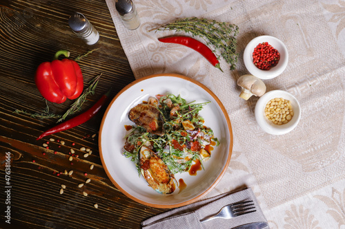 On a dark countertop, a light linen napkin, on a cutting board  Salad with mussels, rucola, red caviar, shrimps in a round dish, cutlery, pepper-salt steam, whole red pepper, hot pepper pod
