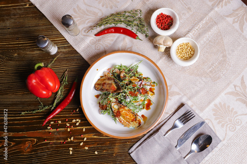 On a dark countertop, a light linen napkin, on a cutting board  Salad with mussels, rucola, red caviar, shrimps in a round dish, cutlery, pepper-salt steam, whole red pepper, hot pepper pod