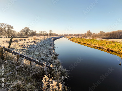 Kanal im Winter mit einer glatten Wasseroberfläche und Frost auf dem Deich