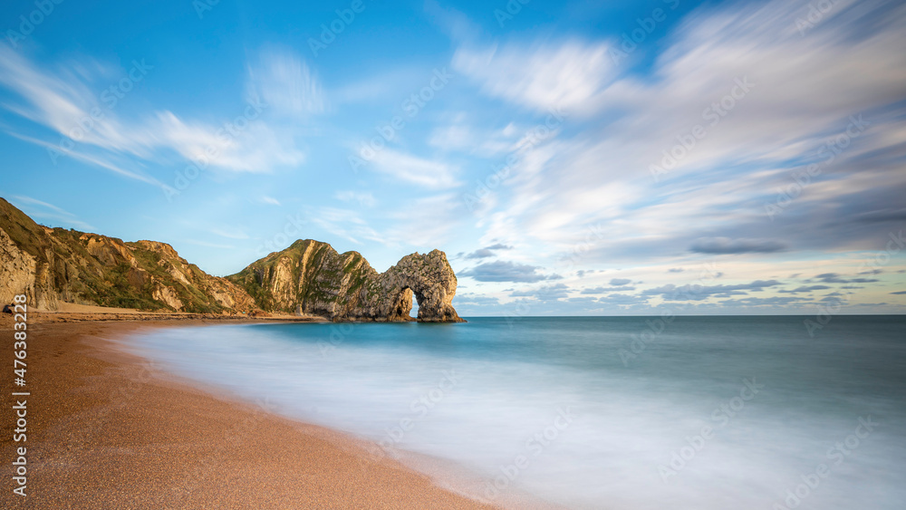 Durdle Door, in Dorset, on the South coast of England.  The natural rock arch is a famous landmark. Slow shutter speed to smooth out the water and the clouds