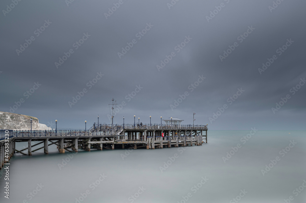 The pier at Swanage, Dorset, on the south Coast of England.  The day is overcast. A long shutter speed has been used to smooth the water and the clouds