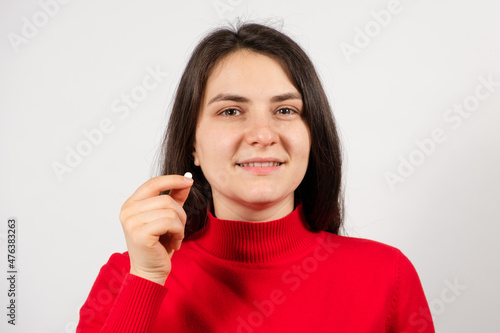 A woman holds a pill in her hand on a white background. Treatment of diseases, dietary supplements and pharmacology