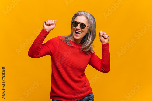 Horizontal portrait of hilarious senior woman in sunglasses dancing isolated on yellow. Middle-aged gray-haired lady celebrating holidays
