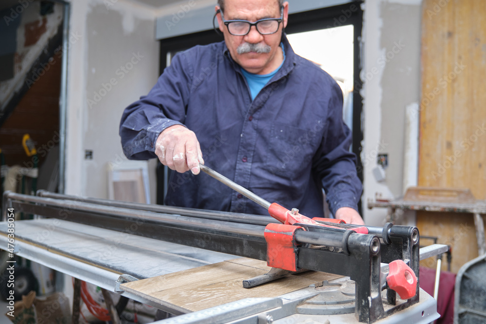 Senior contractor cutting a ceramic wood effect tile with a manual tile cutter. Senior contractor cutting a ceramic wood effect tile with a manual tile cutter.
