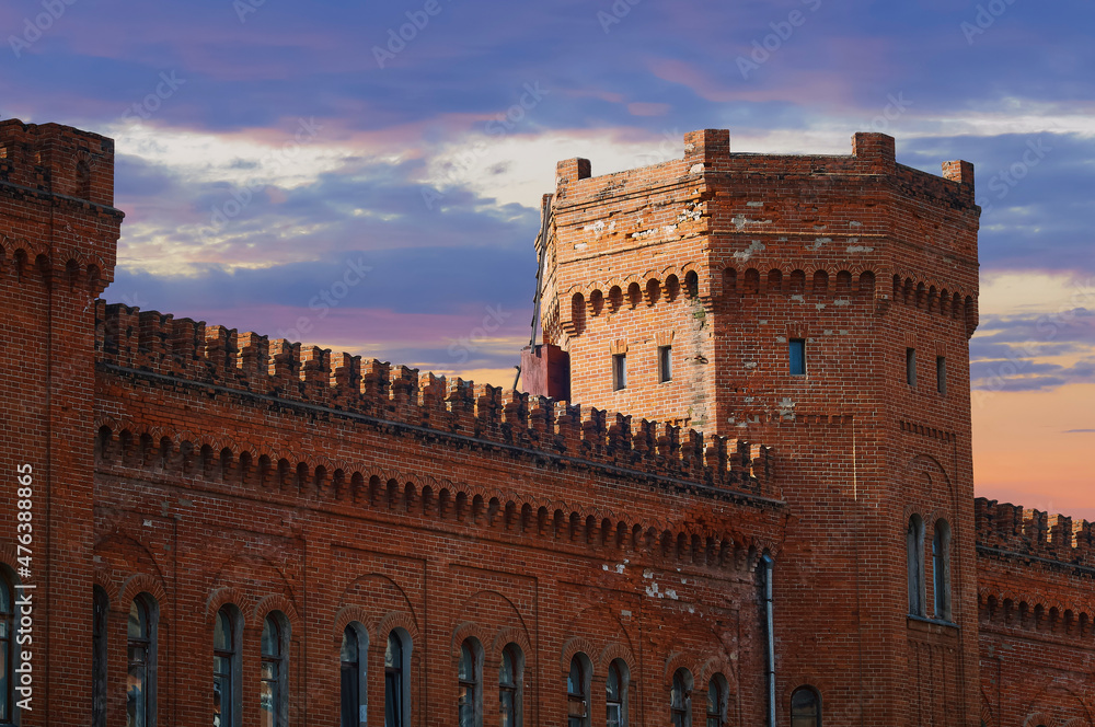 The tower of the fortress is made of red brick. Old town building in medieval style. Breaking down the walls. Redecorating. Dramatic sky with clouds at sunset. Blagoveshchensk, Russia.