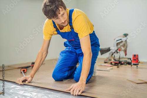 Man installing new wooden laminate flooring on a warm film floor. Infrared floor heating system under laminate floor