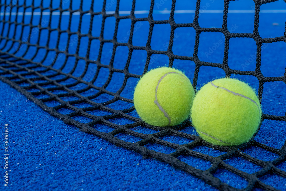 Net of a blue paddle tennis court and two balls