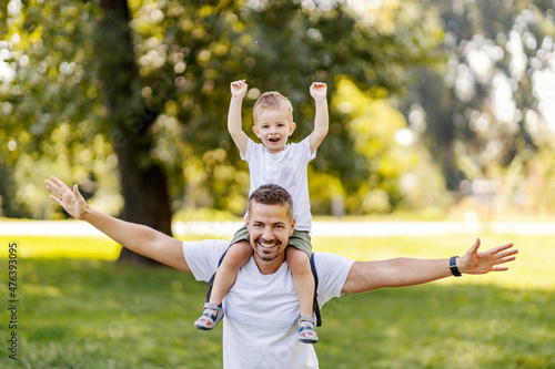 Father and son play in nature. They imagine planes while Dad carries the boy on his shoulders. They have fun and have fun in the park  the same casual clothes. Nice family moment