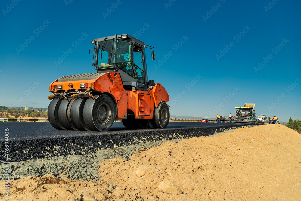 The roller is rolling a hot layer of asphalt against the background of an asphalt paver The roller is rolling a hot layer of asphalt against the background of an asphalt paver