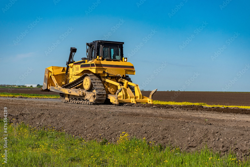 Large crawler bulldozer tears down asphalt from the old road, prepares the way for the recycler to work.