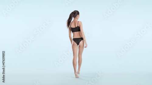 Horizontal shot of young slim cute Asian dark-haired woman with long ponytail in black bikini turns to the camera smiling wide and goes away on tiptoes on pale blue background | Hair removal concept photo