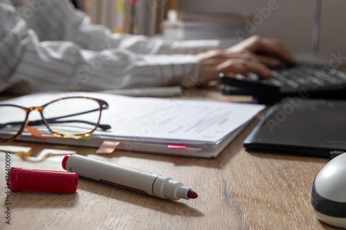 Photos Closeup of red marker, pile of paper,glasses and woman working on computer