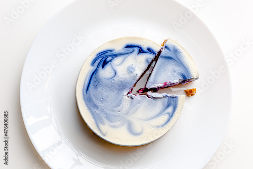 Piece of blue and white cheesecake with blueberry, cherry and black currant sauce inside on white plate on white table