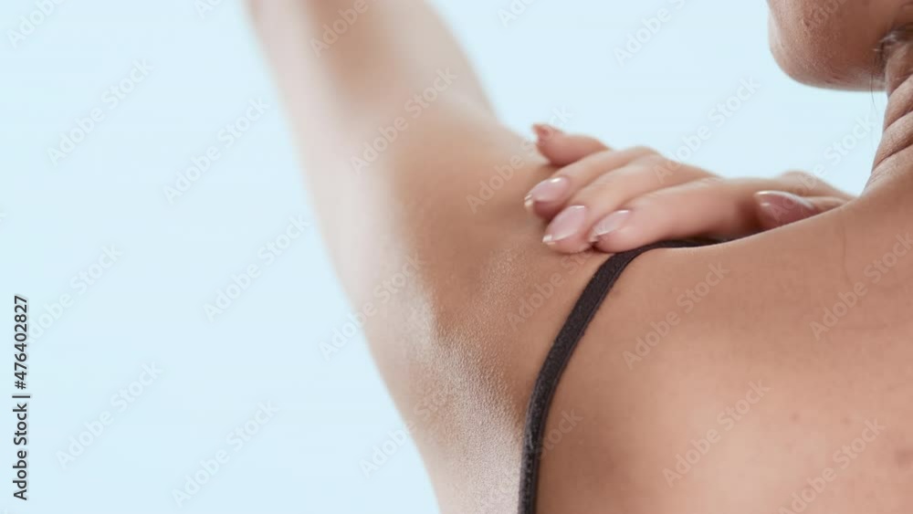 Slim young good-looking female model in black bra touches her raised up hand and shoulder on pale blue background | Skin moisturizing commercial Slim young good-looking female model in black bra touches her raised up hand and shoulder on pale blue background | Skin moisturizing commercial