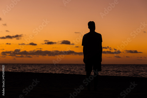 Man standing on a tropical beach at twilight silhouetted against a vivid orange ocean sunset