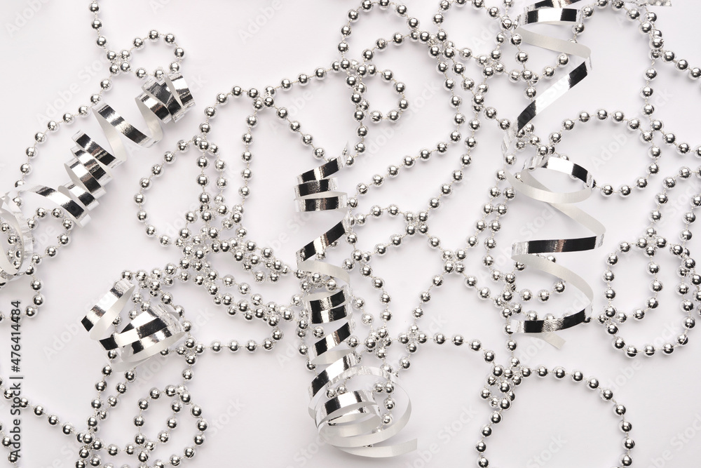 Obraz premium Shiny silver ribbons and beads on a white backdrop. Beautiful monochrome abstract allegory of a selebration