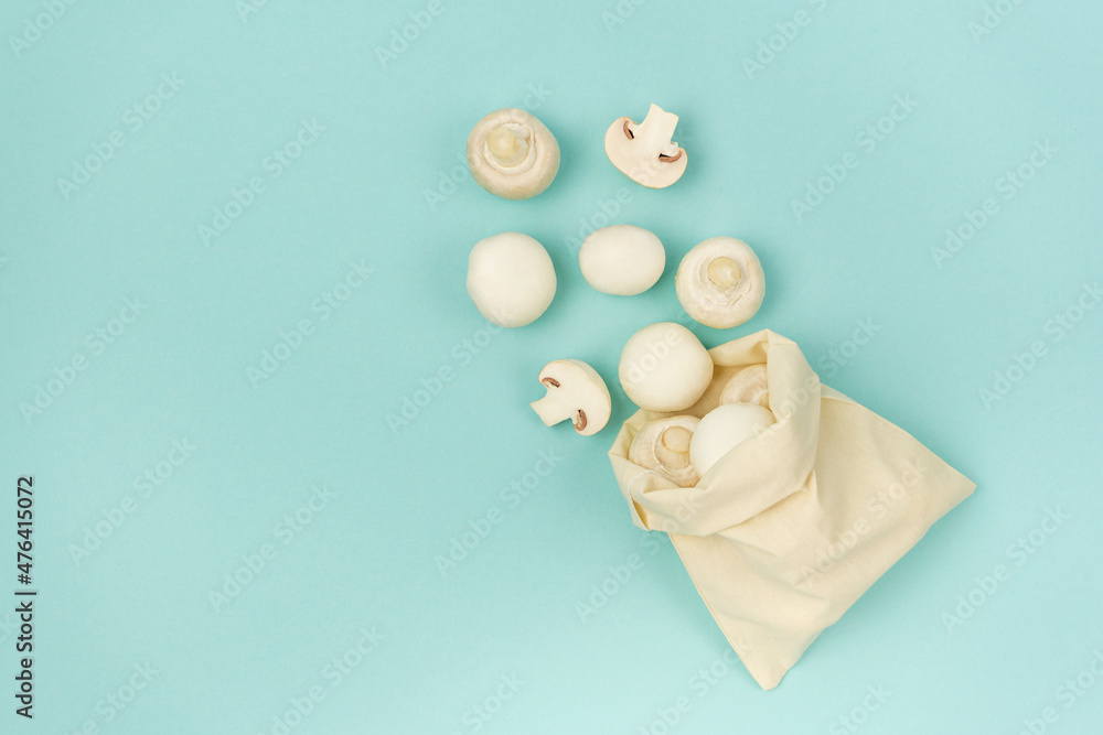 Champignon mushrooms scattered from a fabric bag on a blue background with copy space. top view.