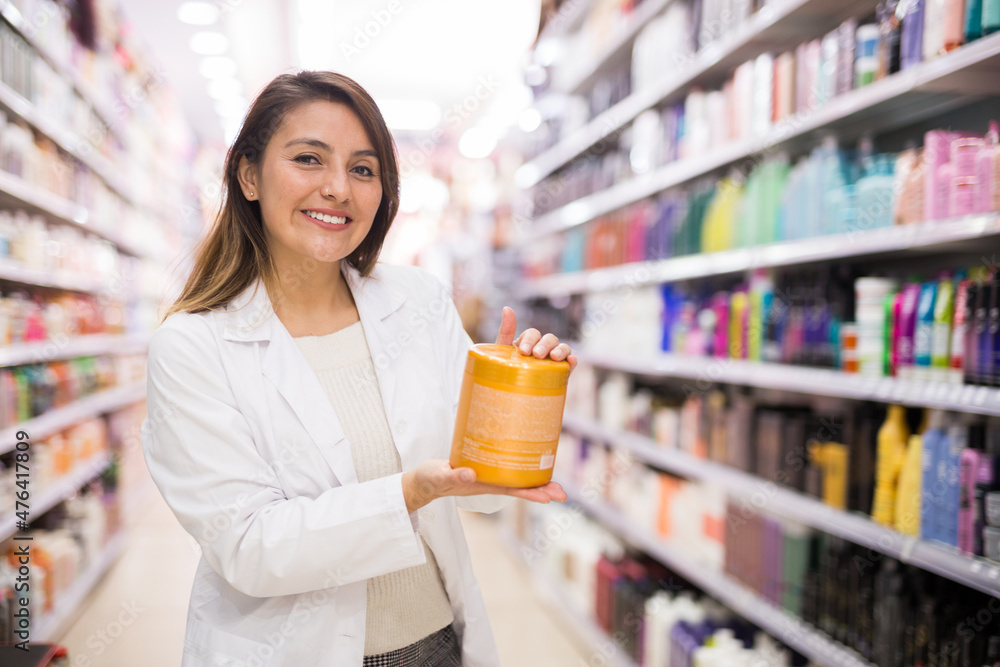 Cheerful saleswoman offering hair care products in cosmetic shop Cheerful saleswoman offering hair care products in cosmetic shop