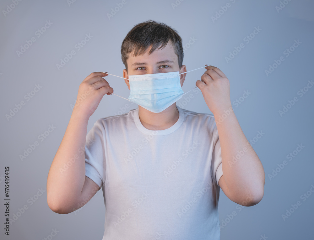 A young man puts on an antiviral protective mask to protect others from the coronavirus infection COVID-19 and SARS cov 2. On a gray background copy space A young man puts on an antiviral protective mask to protect others from the coronavirus infection COVID-19 and SARS cov 2. On a gray background copy space