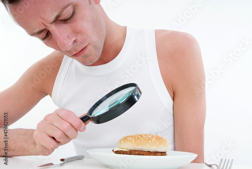 Mann kontrolliert mit Lupe Burger am Teller photo