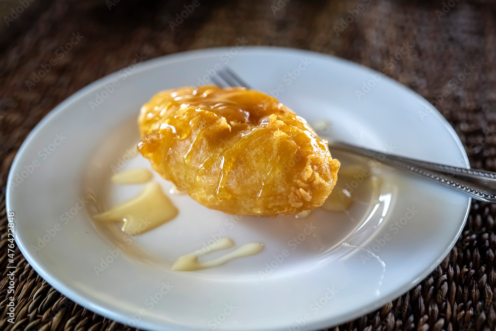 Deep fried banana fritters topping with honey on the white plate on wooden table Deep fried banana fritters topping with honey on the white plate on wooden table