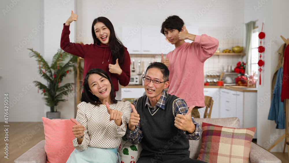 cheerful father. mother. adult daughter and son looking at camera and making thumb victory hand signs while taking burst shots at home during chinese spring festival cheerful father. mother. adult daughter and son looking at camera and making thumb victory hand signs while taking burst shots at home during chinese spring festival