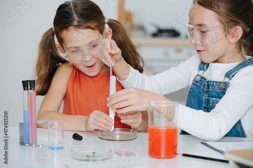 Canvas Print Amased little girls doing science project, one is adding liquid from pipette into a flask, provoking a chemical reaction, release of a gas with a lot of foaming