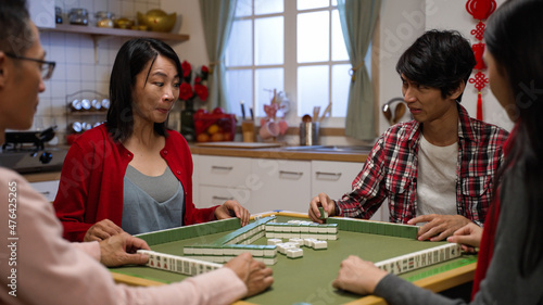 mother clothing making eye gesture to her son for the wanted tile while they are cheating together in mahjong game at home on chinese lunar new year's eve