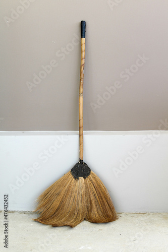 A broom leaning against a gray concrete wall.