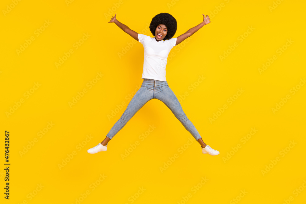 Full length photo of impressed cute dark skin woman dressed white t-shirt smiling jumping high like star isolated yellow color background