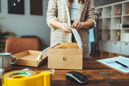 Women, owener of small business packing product in boxes, preparing it for delivery. Young woman selling products online and packaging goods for shipping.  photo