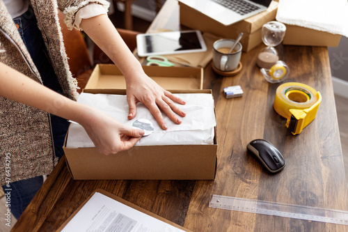 Young woman selling products online and packaging goods for shipping. Women, owener of small business packing product in boxes, preparing it for delivery.