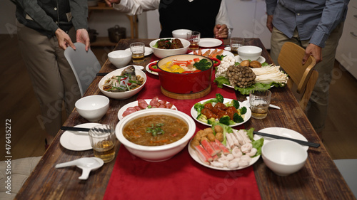 cropped view of senior host of family grandfather clapping hands and gesturing members to sit down at dining table. people pulling out chair, starting to eat big meal for chinese new year
