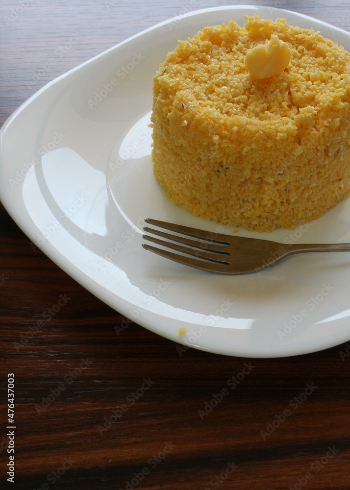 Brazilian couscous in a white plate with fork on the rustic table. Breakfast in Brazil.