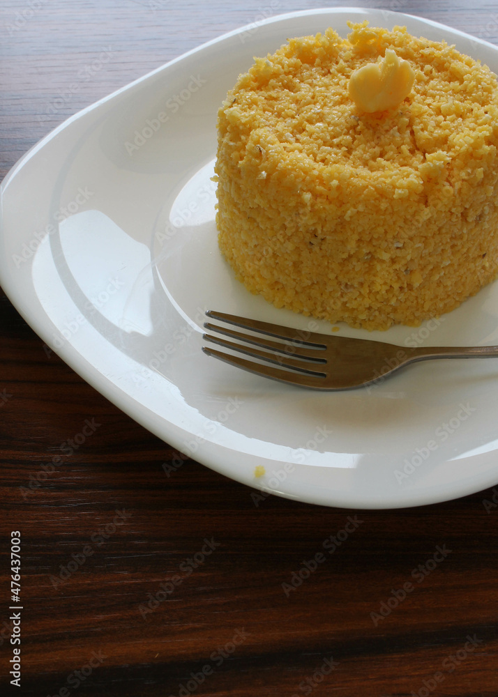 Brazilian couscous in a white plate with fork on the rustic table. Breakfast in Brazil. Brazilian couscous in a white plate with fork on the rustic table. Breakfast in Brazil.