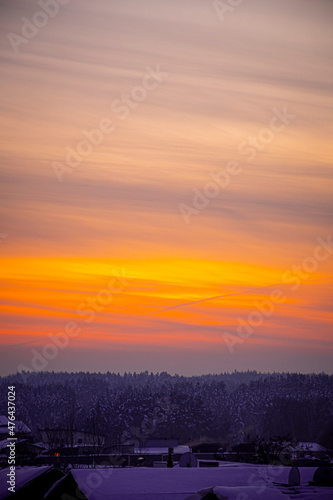 Bright orange sky over a village. Vivid colors of sunset in winter. Colorful vertical cloudscape. Selective focus on the details, blurred background.