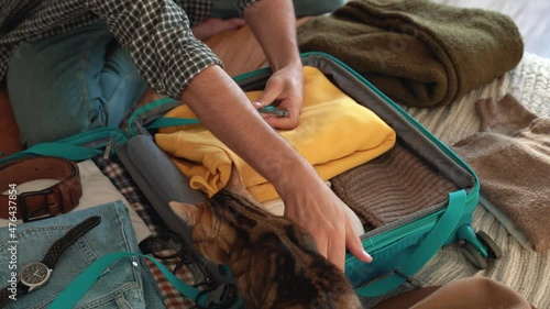 Beardly man getting ready for travel, packing clothes and tablet in a blue suitcase and petting cat. the most necessary things before the trip. Concept of traveling, adventure. 4k footage