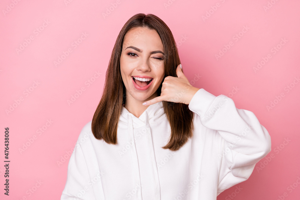 Photo of young girl happy positive smile wink eye show fingers call talk phone sign isolated over pink color background Photo of young girl happy positive smile wink eye show fingers call talk phone sign isolated over pink color background