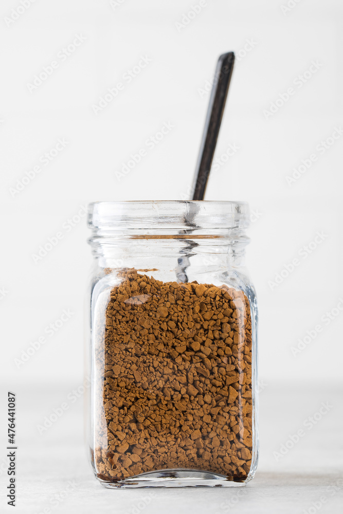 Glass jar with instant coffee with a spoon on a light background.