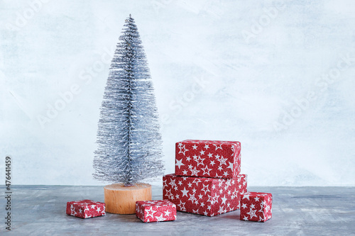 Composition with silver artificial Christmas tree and red Christmas gift boxes on gray background with copy space. © Nadezhda Zaitceva