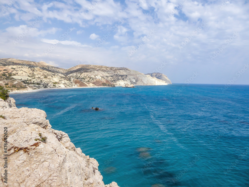 A rocky Aphrodite's beach in Petra tou Romiou, Cyprus. Beach stretches far away, surrounded by steep cliffs. Water has a turquoise shade. Idyllic and calm place. Waves slowly wash the shore