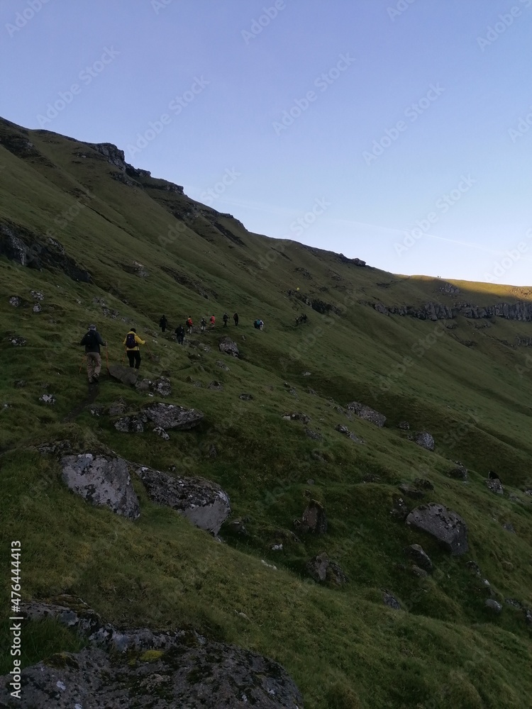 A group of hikers on a green mountain ridge walk in the Faroe Islands