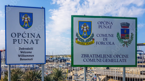 Punat/Croatia-04302018: Two signs welcoming you to enter the territory of Punat. Both of them present the emblem of the city. Sign on the left welcoming the visitors in many languages. photo