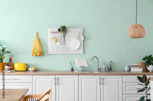 Photo Interior of stylish kitchen with white counters and hanging peg board on green w